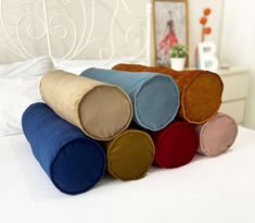 four different colored pillows stacked on top of each other in front of a white bed