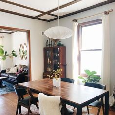 a dining room table and chairs in front of a window with potted plants on it