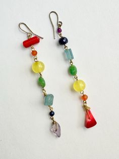 a pair of dangling earrings with multi colored beads and charms on them sitting on a white surface