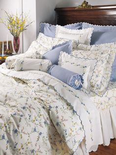 a bed with blue and white comforters in a room next to a dresser filled with flowers