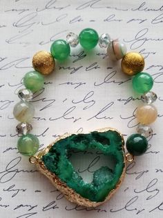 Give your wrist a bold, natural shine with the addition of beautiful crystals! Eclectic in style, this beautiful open green dyed agate pendant offers an irregular shaped druzy cluster with metallic edges of gold foil. The pendant is a great  focal on this bracelet. The druzy is 1.5 inches (1.25 inches in width). The green druzy ia accompanied by green and brown agate rounds, along with facet crystal rondelles. The agate rounds and crystal mixture has swirling patterns and shining facets. The bra Gold Agate Crystal Bracelet For Healing, Green Bohemian Beaded Bracelets With Stones, Bohemian Green Beaded Bracelets With Stones, Bohemian Green Beaded Bracelets, Green Beaded Bracelets With Healing Stones, Green Beaded Bracelets For Healing, Green Healing Stones Beaded Bracelets, Elegant Green Agate Crystal Bracelet, Elegant Green Crystal Bracelet With Natural Stones