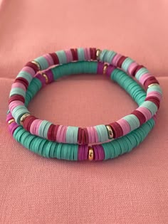 three bracelets with different colored beads on a pink cloth covered surface, close up