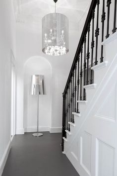 an elegant chandelier hangs from the ceiling in this white hallway with black railings