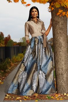 a woman standing next to a tree with leaves on the ground in front of her