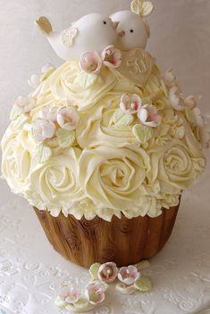 two birds sitting on top of a cupcake covered in white frosting and flowers