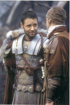 a man in armor talking to another man wearing a fur collared hat and cape