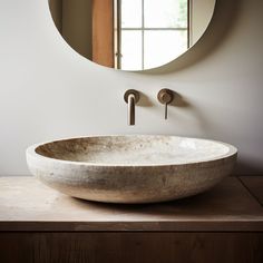 a round sink sitting on top of a wooden counter in front of a circular mirror