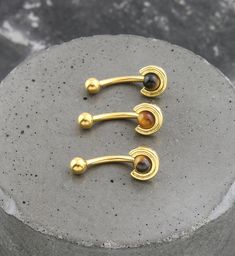 three gold - plated ear hooks with black and brown beads on top of a stone slab