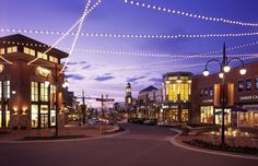 an empty street at night with lights strung across the road and buildings in the background