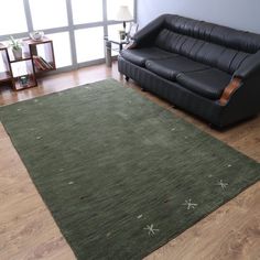 a living room with a black leather couch and green area rug on the hardwood floor