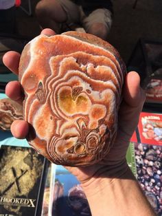 a person holding a rock in their hand with other books behind it on the table