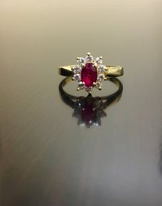 a close up of a ring with a red and white stone in the center on a reflective surface