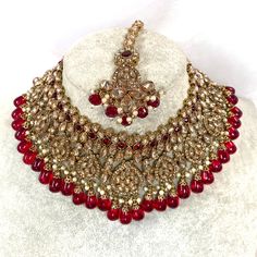 Beautiful antique gold necklace set with dazzling champagne zircon crystals and maroon stones. Plus maroon glass beads. Perfect bridal set Comes with matching jhumka earrings and matching tikka! Necklace 3 inch with adjustable string Earrings 2.25 Inch including jhumka length x 1 inch width Tikka 2.5 inch pendant plus 2 inch chain and 2 inch extender chain  Ready to be shipped ❤️ Gold Beaded Necklace With Stone Work For Festive Occasions, Ornate Gold Necklaces With Stone Work, Gold Crystal Bridal Necklace For Celebrations, Gold Beaded Necklaces With Stone Work For Wedding, Gold Jeweled Bollywood Bridal Necklace, Gold Bollywood Beaded Jewelry, Festive Gold Beaded Necklaces With Stone Work, Gold Crystal Kundan Necklace For Celebration, Gold Beaded Ruby Necklace