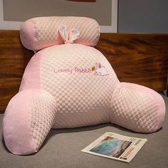 a pink teddy bear sitting on top of a bed next to a magazine and lamp