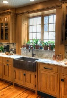 a kitchen with wooden cabinets and marble counter tops, along with potted plants on the window sill