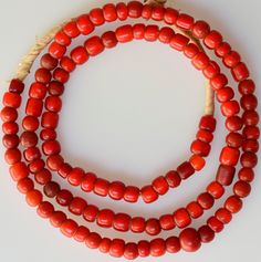 three strands of red coral beads on a white surface with a rope attached to it