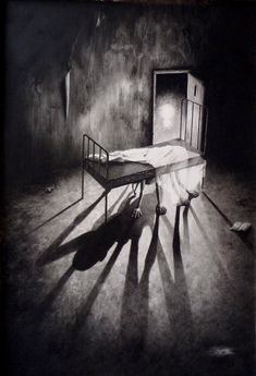 a black and white photo of a bed in a dark room with shadows on the floor