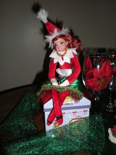 an elf sitting on top of a box with wine glasses in front of it and other decorations