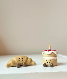 two small clay animals sitting next to each other on a white counter top, one wearing a birthday hat and the other as a cake