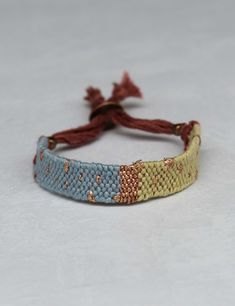 a blue and yellow woven bracelet with tassels on white table top next to red string