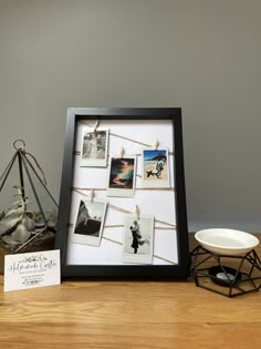 a wooden table topped with pictures and a white bowl filled with flowers next to a black frame