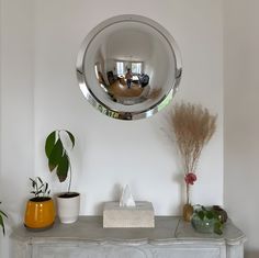 a mirror is hanging on the wall above a table with potted plants and other items