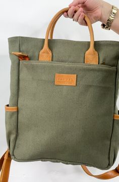 Zelaki Leather Co Canvas Backpack in Olive The Canvas Backpack is a durable and gender-neutral bag that can serve many purposes. With its sturdy design, it can withstand daily wear and tear, making it a reliable choice for those on the go. Details: -Ethically & sustainably made in Ethiopia-Canvas & full-grain leather-Canvas interior-One outside zipping pocket (12"x12") -Zipper closure -Two cupholders -One interior compartment (13"x12")-Adjustable straps-15"H x 12"W x 4"D Khaki Large Capacity Shoulder Backpack, Khaki Satchel Backpack With Large Capacity, Khaki Satchel With Top Carry Handle For Daily Use, Khaki Backpack For Daily Use, Practical Backpack For On-the-go, Khaki Large Capacity Satchel For Everyday Use, Khaki Travel Bag With Top Carry Handle, Khaki Backpack For Everyday Use, Green Canvas Backpack For Travel