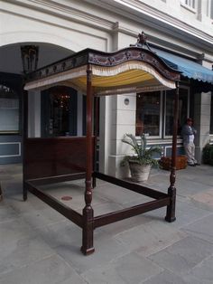 a wooden bed sitting on top of a sidewalk next to a tall white building with a blue awning