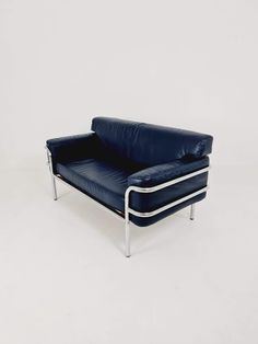 a blue leather sofa with chrome legs and arm rests against a white wall in an empty room