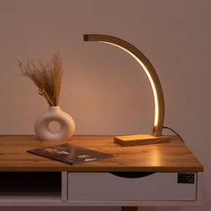 a white vase sitting on top of a wooden table next to a light that is turned on