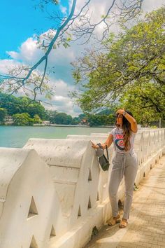 a woman standing on the side of a bridge next to a body of water with trees in the background