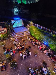 an aerial view of people sitting at tables in the middle of a courtyard with lights strung across it