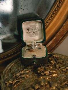 an open ring box with a diamond in it sitting on top of a table next to a mirror