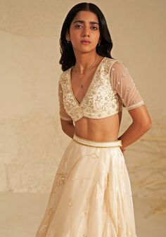 Featuring a beautiful cream lehenga made from shimmering metallic organza fabric, creating an ethereal glow. This elegant set comes with a matching blouse featuring delicate aari hand embroidery, adding a touch of intricate detail. A flowing silk organza dupatta completes the look, draped softly to highlight the outfit's timeless grace. Ideal for a reception at a destination wedding, this ensemble captures the heart with its simple beauty and elegance. Composition : Lehenga, Blouse, Dupatta - Organza Care: Dry Clean Only and Vacuum Storage This product can be customized for sleeves, length of blouse and neckline Delivery : 4-6 weeks as the product is hand crafted. Check Size Guide or choose MySize for free customisation (All Sizes above XL can be made at 15% additional cost) For more infor Elegant Off-white Lehenga For Festive Occasions, Elegant Off White Choli For Festive Occasion, Party Choli In Cream With Intricate Embroidery, Party Cream Choli With Intricate Embroidery, Elegant Off White Festive Choli, Elegant Cream Choli With Sheer Dupatta, Gold Fitted Organza Pre-draped Saree, Festive Cream Choli With Sheer Dupatta, Off White Organza Sets With Zari Work