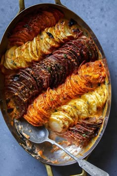 an iron skillet filled with potatoes and meats on a blue table top next to a spatula