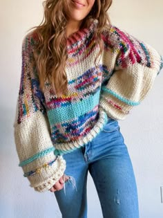 a woman is posing for the camera wearing jeans and a sweater with multicolored stripes