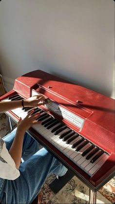 a person sitting at a red piano with their hands on the keys and playing it