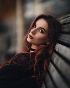 a woman with red hair is leaning on a bench and looking at the camera while she has her eyes closed