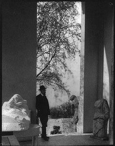 an old photo of two men standing in front of a tree and statues on the ground