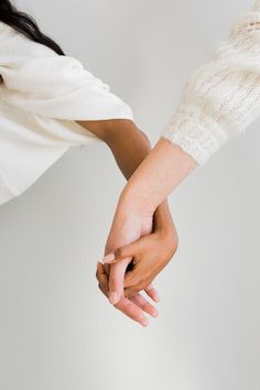 two people holding hands while standing next to each other in front of a white wall