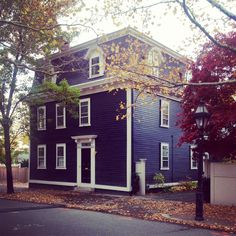 a blue house with white trim on the front and side of it in fall foliage