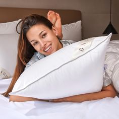 a woman laying on top of a white bed with pillows in front of her face