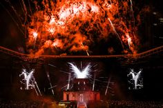 fireworks are lit up in the night sky above a stage with people on it and large red smokestacks