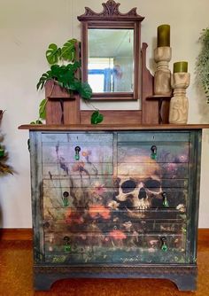 an old dresser with a skull painted on the front and drawers, next to a mirror