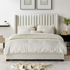 a white bed with two framed pictures above it and a fur rug on the floor