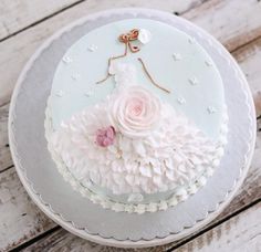 a white cake decorated with pink flowers and a dress on top is sitting on a wooden table