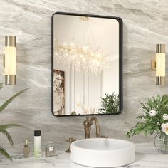 a bathroom with a sink, mirror and lights on the wall next to flowers in vases