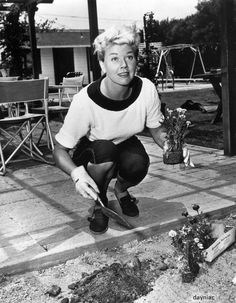 an old black and white photo of a woman kneeling on the ground with gardening tools