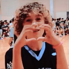 a young boy making a heart with his hands while standing in front of an audience