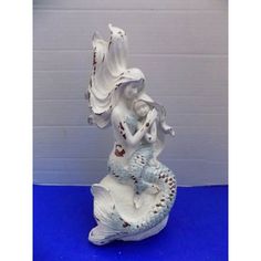 a white ceramic mermaid figurine sitting on top of a blue table next to a wall